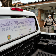 Três brigadianos em frente ao posto do décimo nono batalhão da brigada, seguindo em direção a uma picape da brigada com a inscrição "Patrulha Maria da Penha"