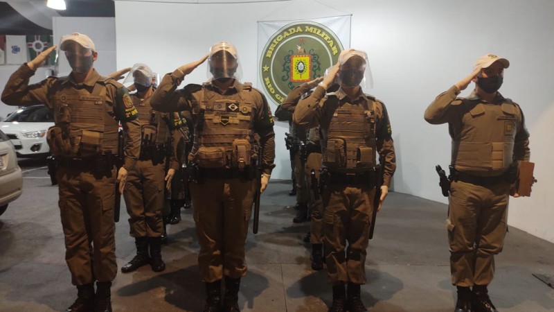Policiais Militares em forma prestando continência ao terreno.