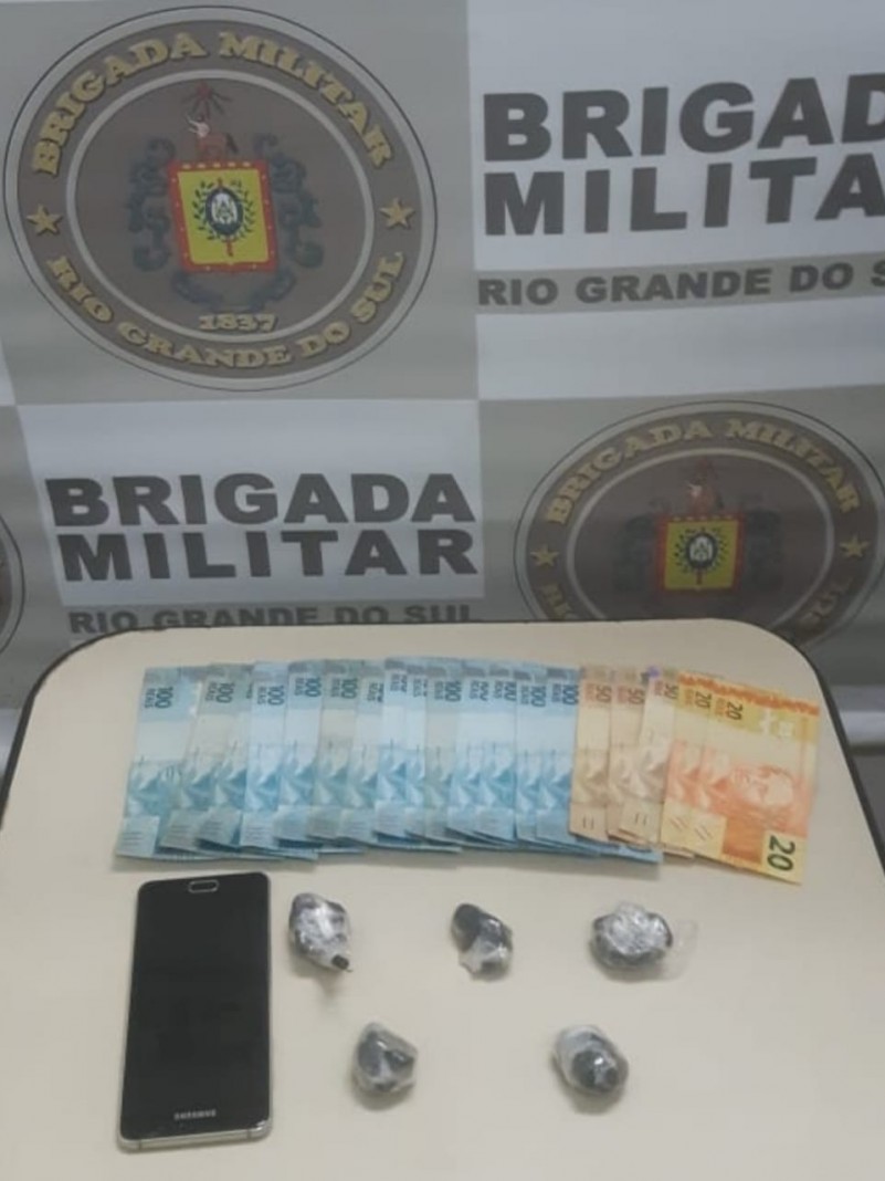 dinheiro, drogas, celular, banner institucional da Brigada Militar