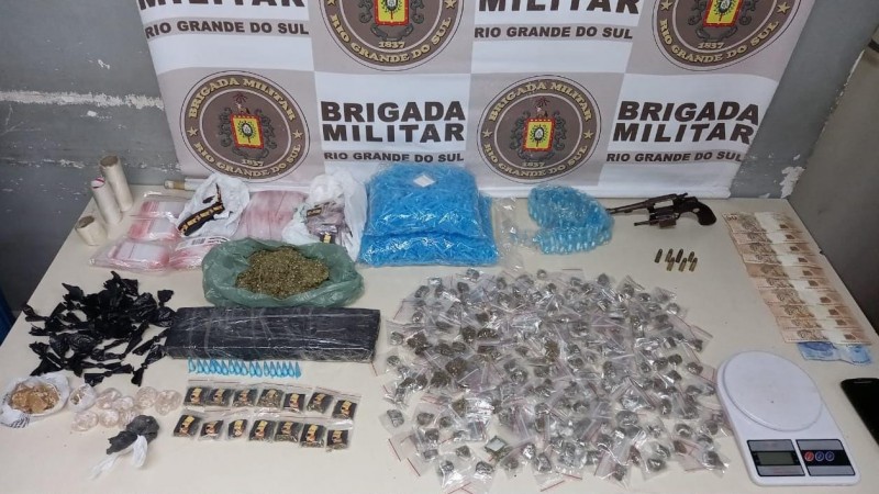 Ao fundo um banner com v&aacute;rios logos da Brigada Militar. Em frente uma mesa com todas as drogas e armas dispostas em cima
