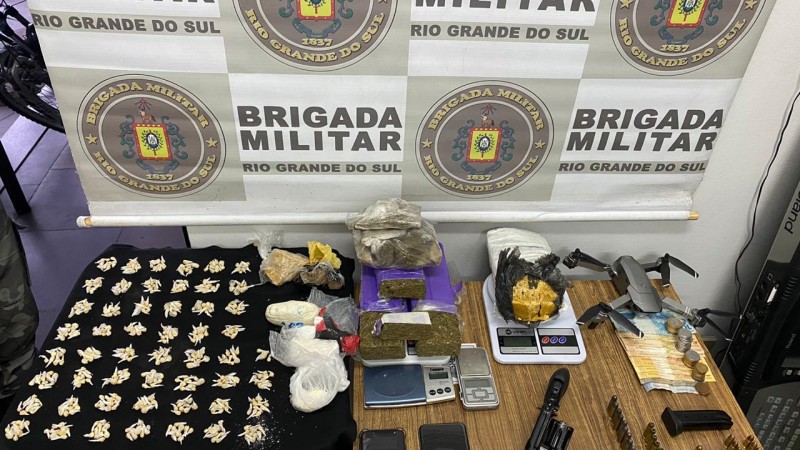 A imagem mostra drogas, arma, muni&ccedil;&otilde;es, dinheiro, balan&ccedil;as de precis&atilde;o entre outros objetos sobre uma mesa.