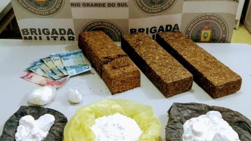 Banner da Brigada Militar ao fundo. Sobre a mesa drogas e dinheiro em esp&eacute;cie.