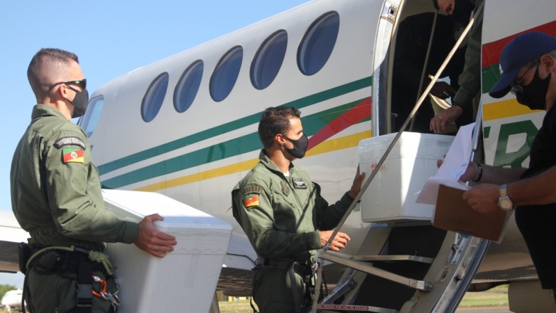 Policias militares do Batalhão de aviação carregando as doses das vacinas para dentro do avião