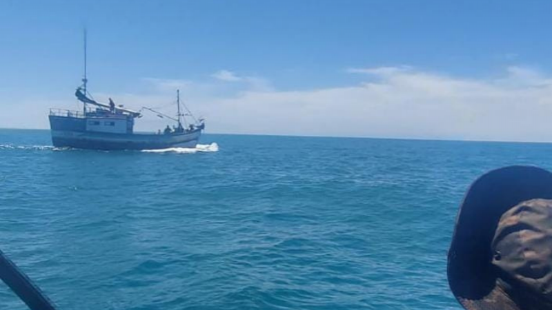 Foto de um barco ao mar e um policial militar fardado olhando para a embarcação