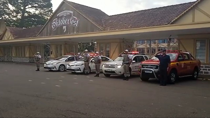 Viaturas da brigada Militar e corpo de bombeiros militares perfilados, com policiais e bombeiros a sua frente prestando continência e com os giros flex ligados.