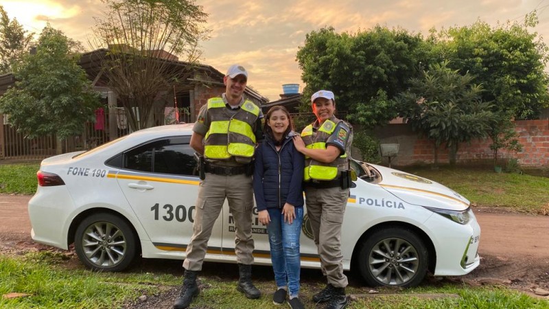 dois militares junto a uma menina na frente da viatura