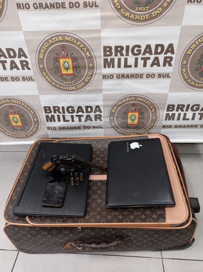 Imagem de um revólver, dois notebooks e uma mala
