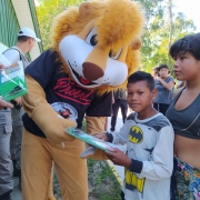 Leão do Proerd entregando um kit para uma criança