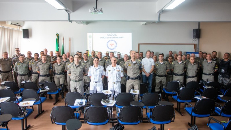 Grupo de militares estão de pé lado a lado em um salão olhando para a câmera