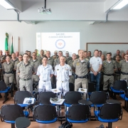 Grupo de militares estão de pé lado a lado em um salão olhando para a câmera