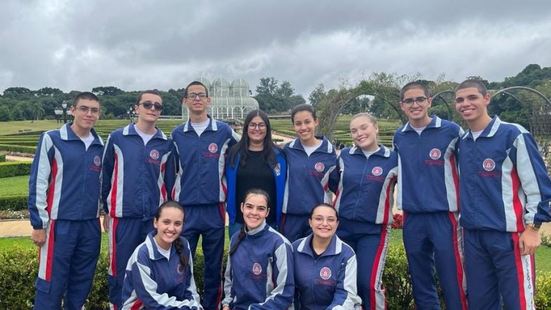 Imagem mostra 10 estudantes e uma professora posando para foto ao ar livre no Jardim Botânico de Curitiba