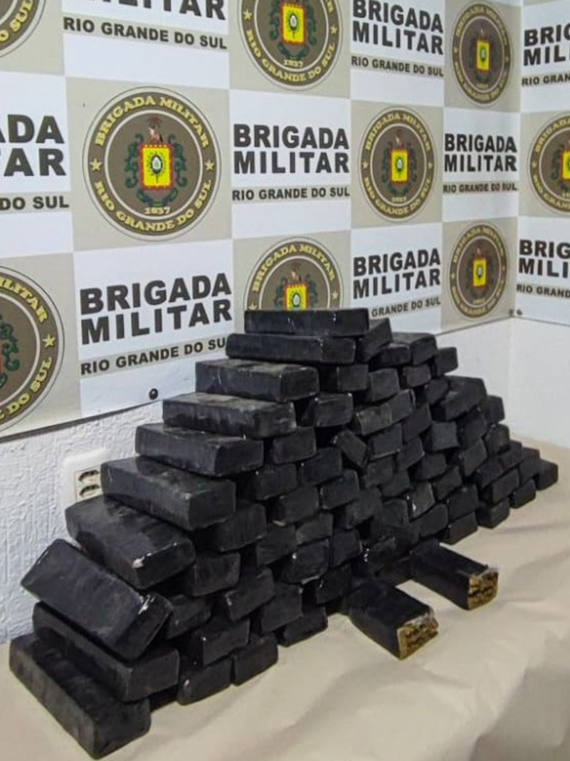 Tijolos de maconha apreendidos, enrolados em fita isolante preta e agrupados sobre uma mesa.