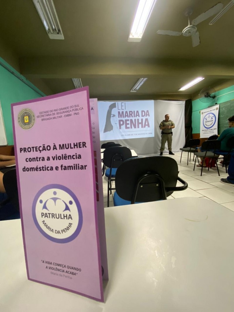Foto mostra panfleto da Patrulha Maria da Penha aberto em cima de uma mesa de sala de aula