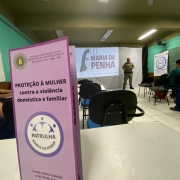 Foto mostra panfleto da Patrulha Maria da Penha aberto em cima de uma mesa de sala de aula