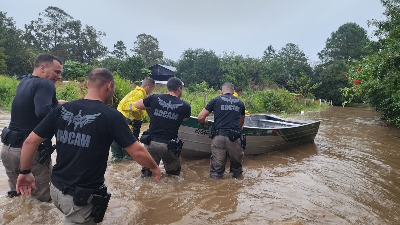 Foto mostra policiais militares empurrando um barco em uma área alagada