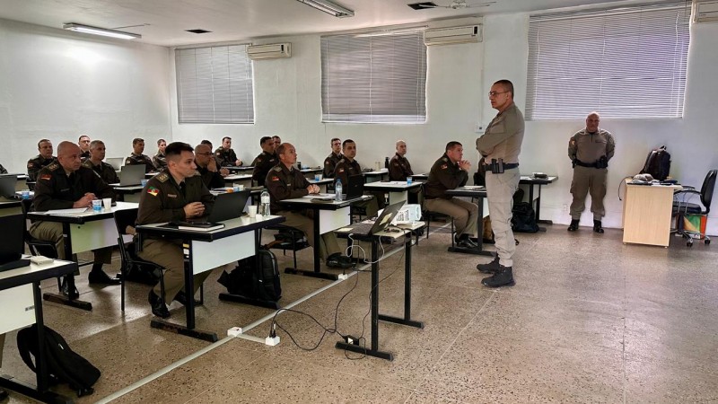 Imagem mostra uma sala de aula com alunos sentados e todos fardados com o uniforme da Brigada Militar.