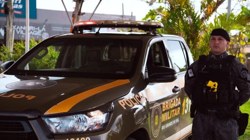 Policial militar do batalh&atilde;o de choque ao lado de uma viatura verde em posi&ccedil;&atilde;o de respeito.