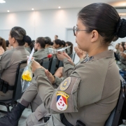 Enquanto as PMs batem palmas, a imagem mostra uma delas, de lado, segurando uma rosa amarela. 
