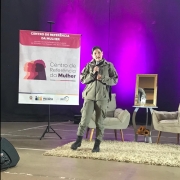PM feminina aparece durante a palestra em um palco iluminado com a cor rosa. 