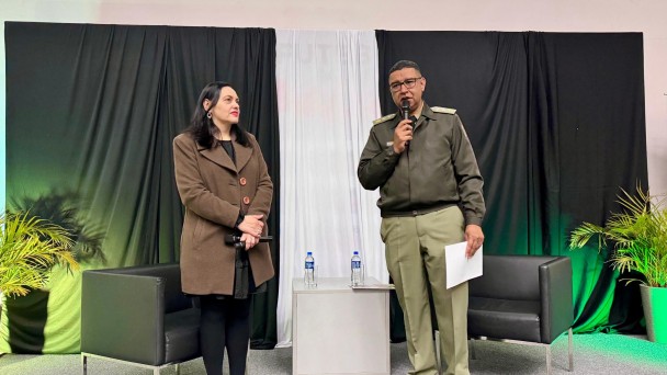 Autoridades aparecem no palco do evento, um homem e uma mulher, ambos seguram microfones. 