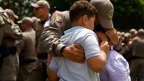 Policial Militar recebe o cumprimento de duas crian&ccedil;as com um abra&ccedil;o emocionado. 